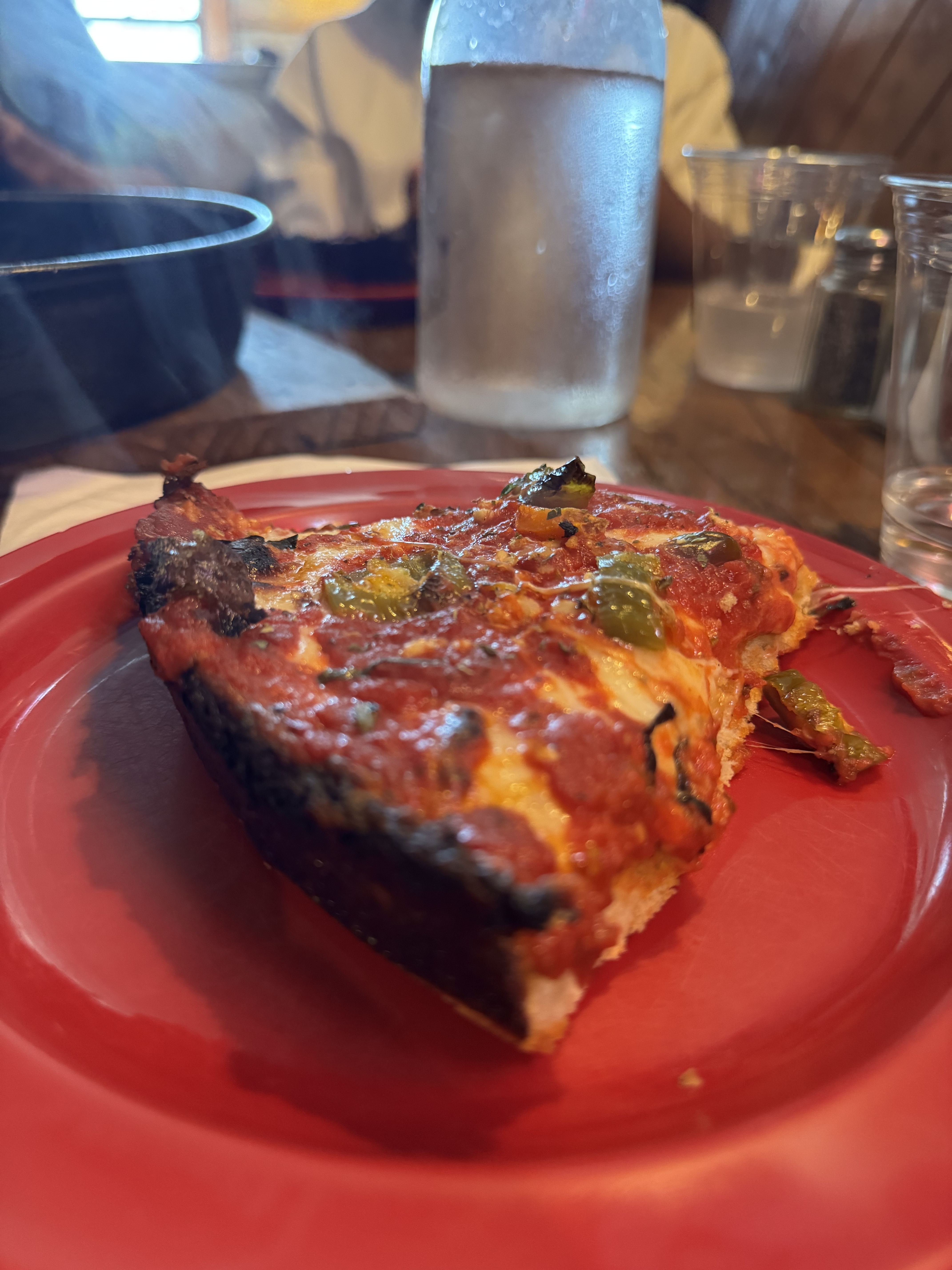 Slice of Pequod's deep dish pizza on a red plate, with a heavily caramelized dark crust edge